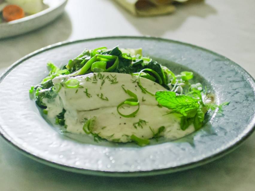 Φιλέτο ψαριού με κρεμώδη σάλτσα, άνηθο, φρέσκο κρεμμυδάκι και φύλλα μέντας σε γκρι πιάτο.